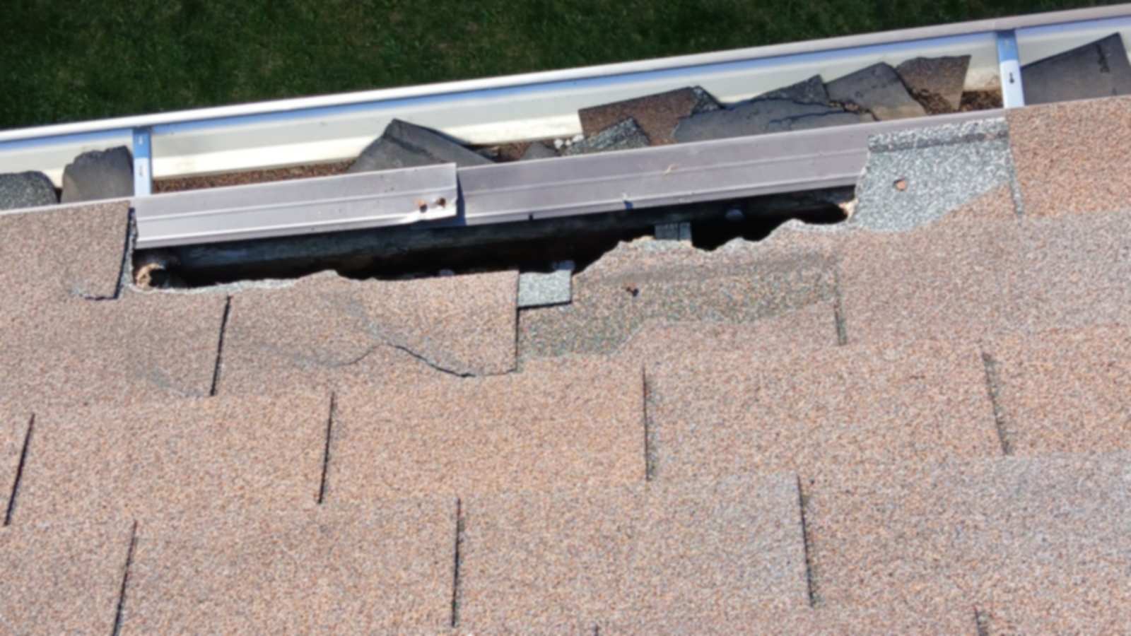 Close view of a roof edge at the gutter where the shingles and metal edging have been torn open.